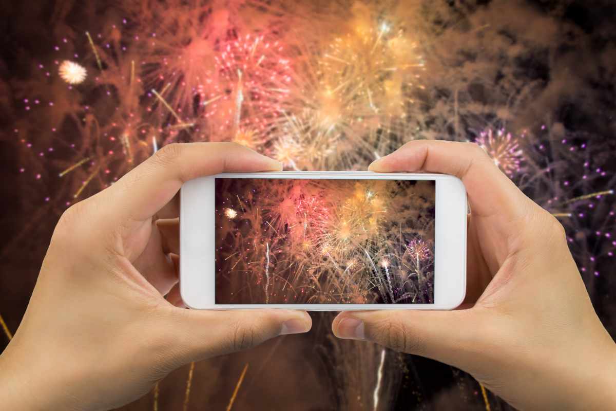 mani reggono smartphone nel fotografare i fuochi d'artificio
