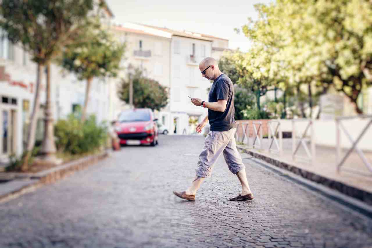 Un uomo che che attraversa una strada restando con la faccia sul cellulare: uno Smombie (Adobe Stock)