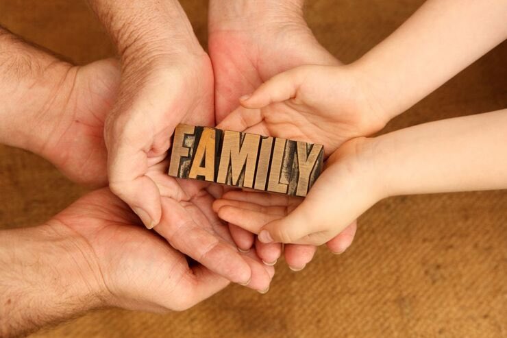 Mani di uomo, donna e bambino con in mano scritta "Family" di legno 