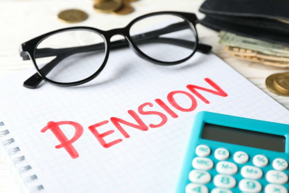 Foglio con scritto in rosso "Pension", calcolatrice azzurra, occhiali da vista, monetine sul fondo