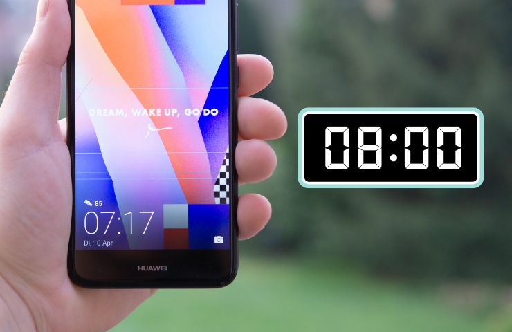 persona che tiene in mano uno smartphone inquadrando l'orario con affianco un orologio digitale che segna le 8:00