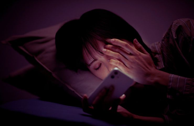 donna che usa lo smartphone di notte con una luce che le illumina il viso