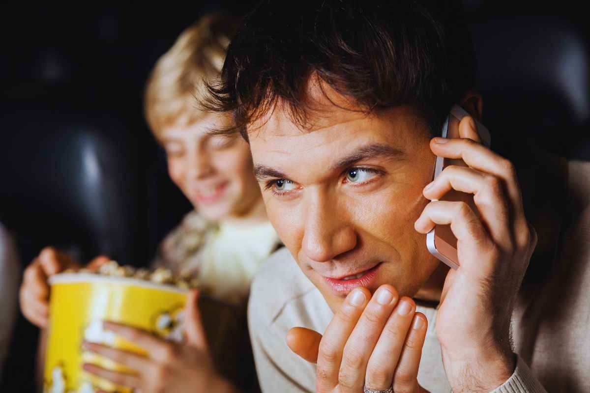 Uomo parla al telefono durante proiezione film al cinema