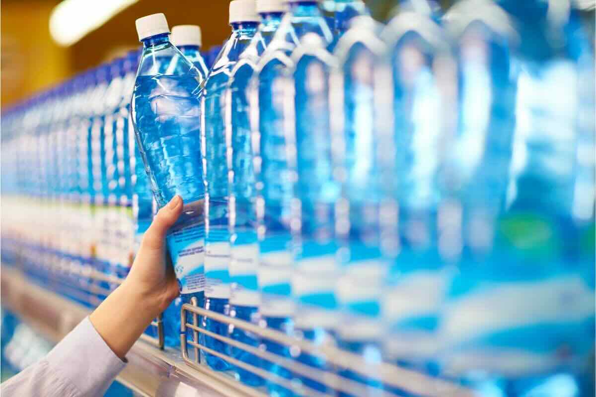 Mano prende una bottiglia di acqua da scaffale con altre bottiglie