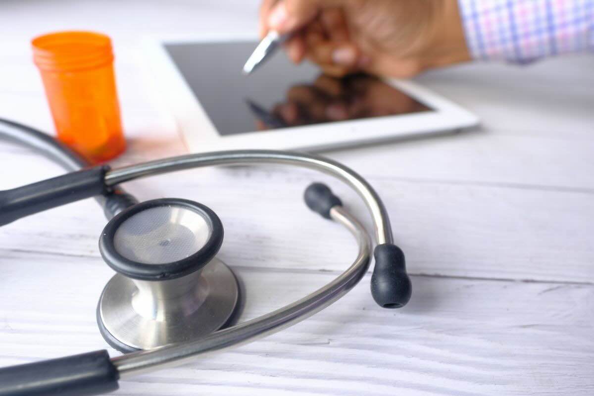Documenti, mano che scrive su tablet, fonendoscopio