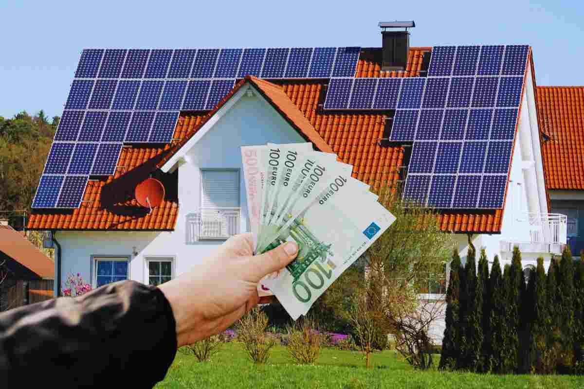 casa con pannelli fotovoltaici e mano con soldi in euro