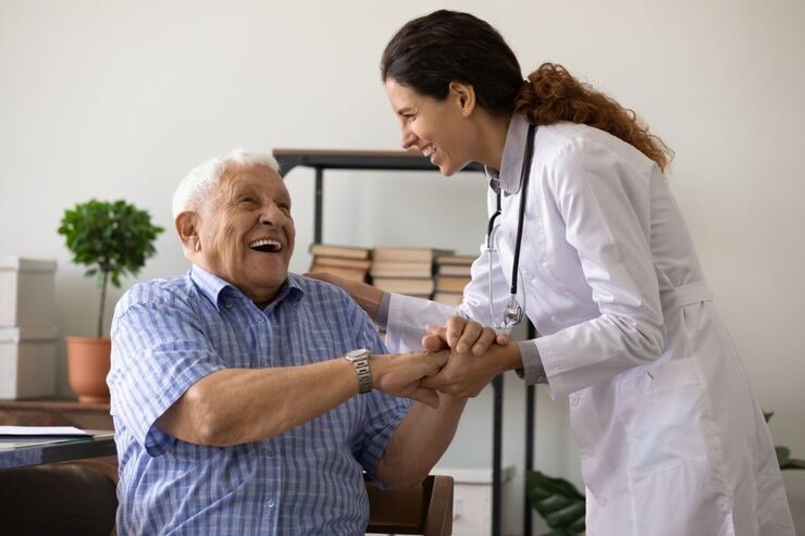 Donna sorridente in camice bianco tiene la mano ad anziano uomo sorridente