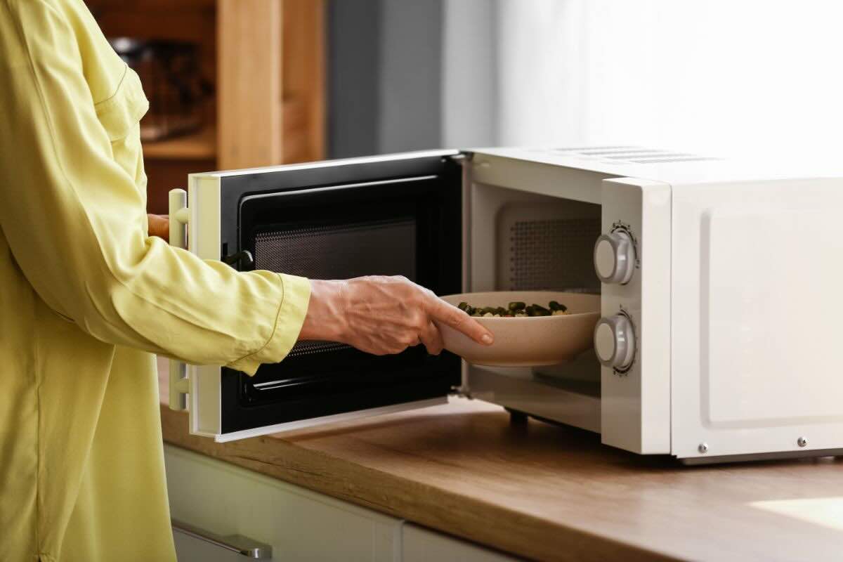 Mano che mette un piatto con cibo nel forno a microonde