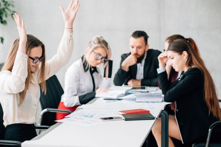 Al lavoro, seduti al tavolo 4 donne e un uomo. Solo una esulta, gli altri hanno il capo basso e sono tristi 