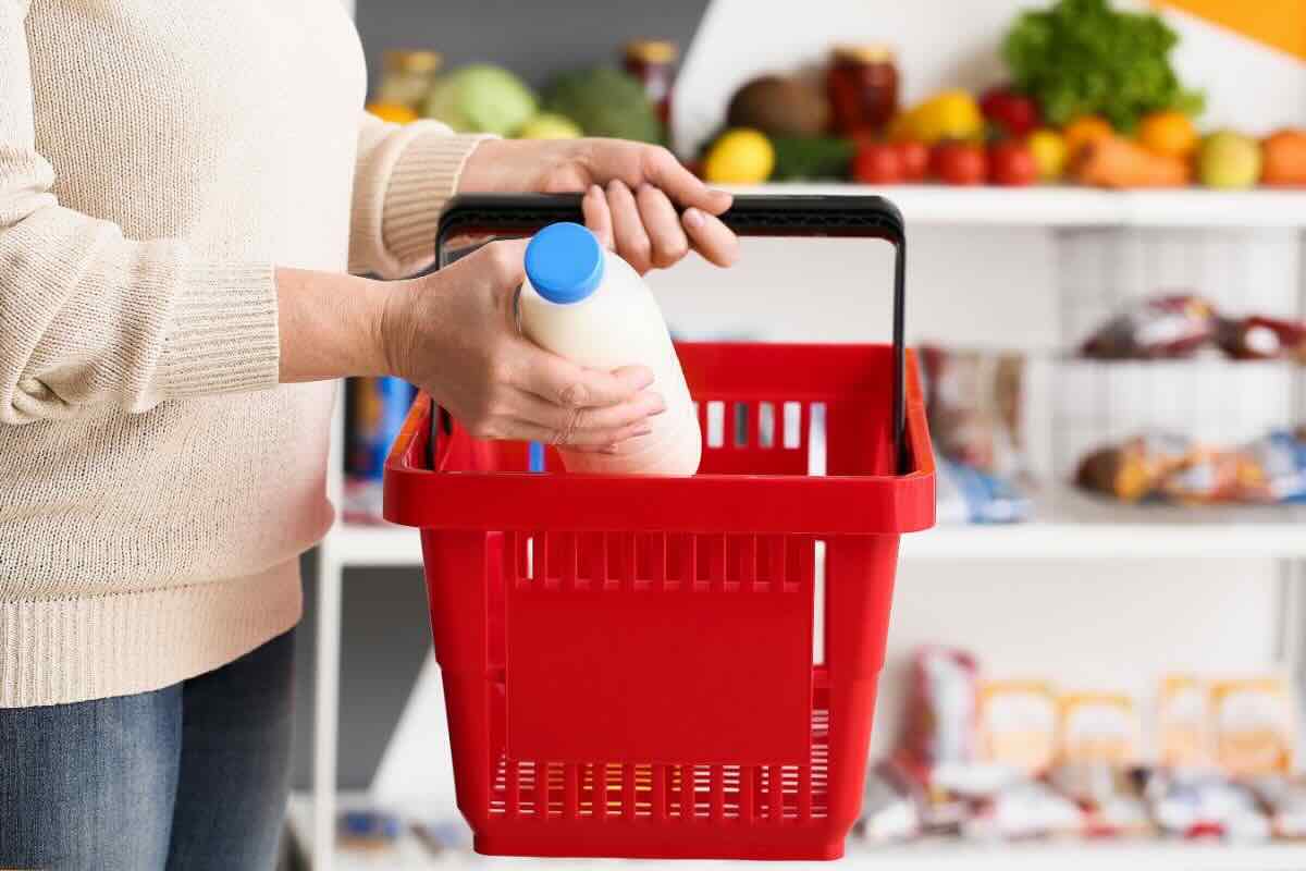 Mani inseriscono latte nel cestino rosso della spesa