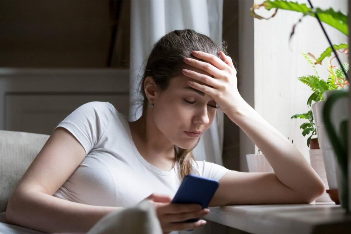 Ragazza con pano sulla fronte, guarda il telefono affranta