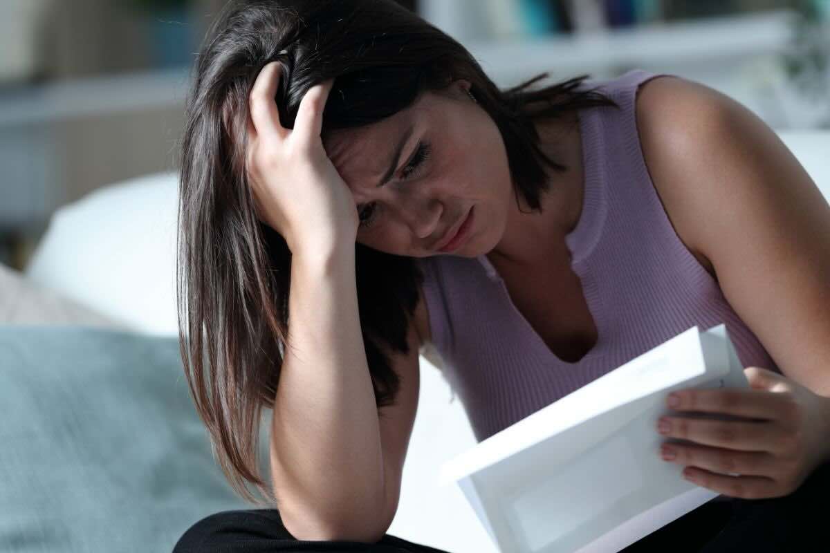Ragazza con mano sulla fronte affranta che legge documento