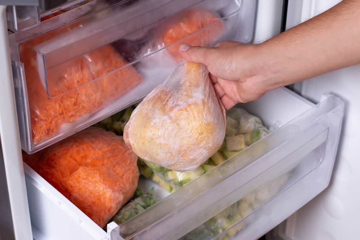 Mano che prende sacchetto con cibo congelato dal freezer