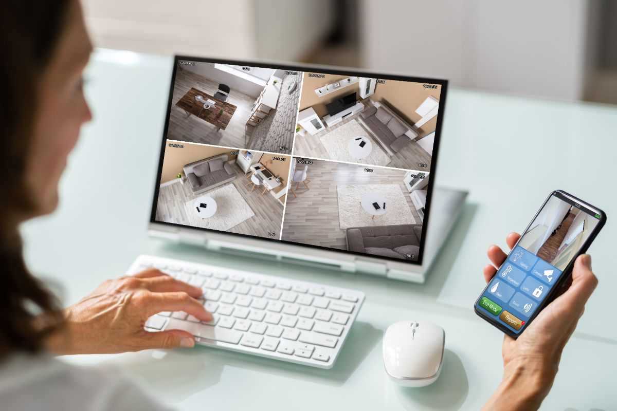 donna che usa lo smaprtone e il pc e controlla le telecamere