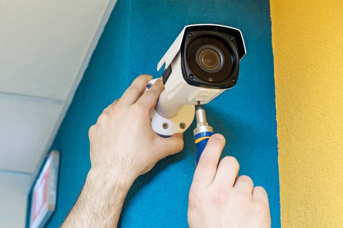 Mani di uomo impiantano telecamera su parete