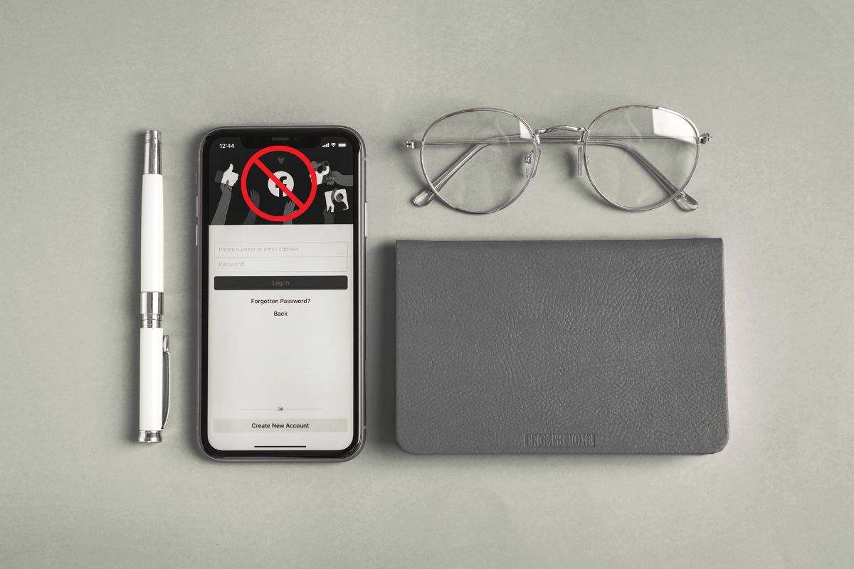 Penna, taccuino, occhiali e smartphone con schermata accesso Facebook su tavolo