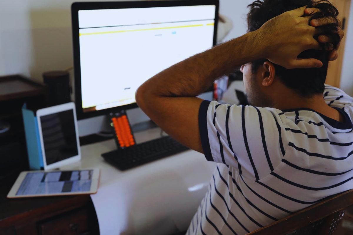 Uomo con le mani sulla testa davanti a monitor bianco