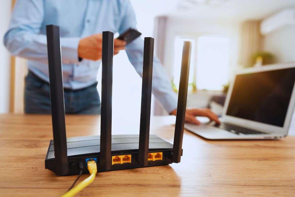 Router e laptop poggiati su scrivania e uomo che si appresta ad accendere il PC
