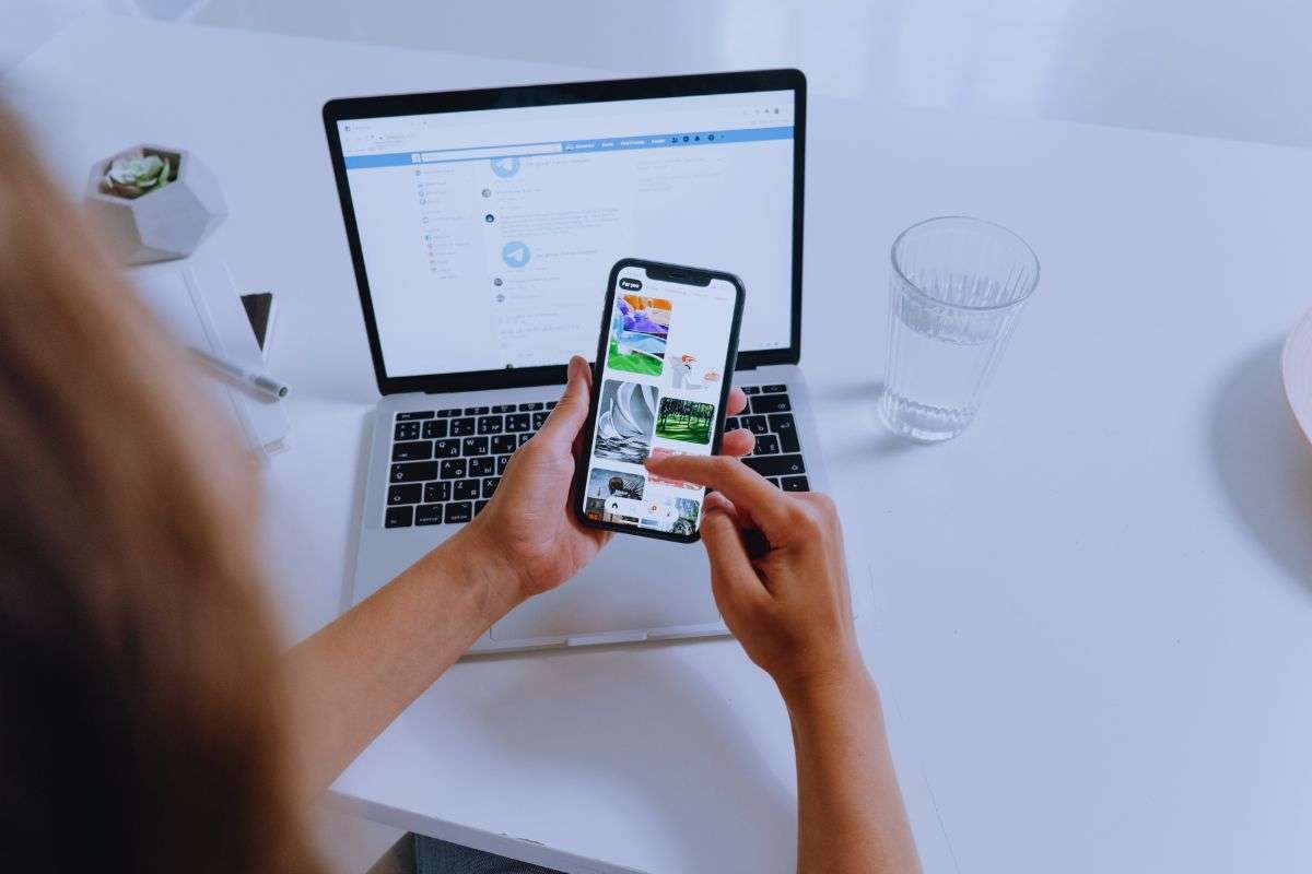 Persona che guarda foto su smartphone, sullo sfondo PC con Telegram Web attivo