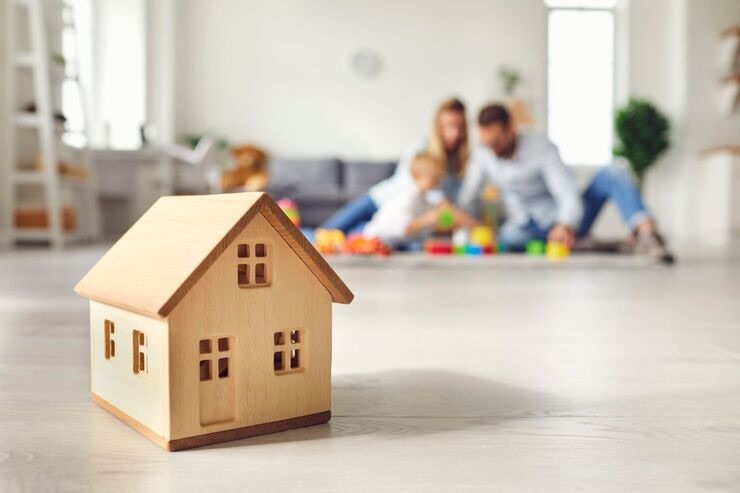 Casetta in legno in primo piano e sul fondo famiglia che gioca (mamma, papà e bambini)