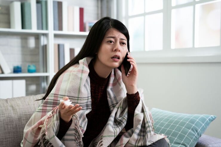 Ragazza sul divano parla al telefono. Plaid sulle spalle e fazzoletto in mano