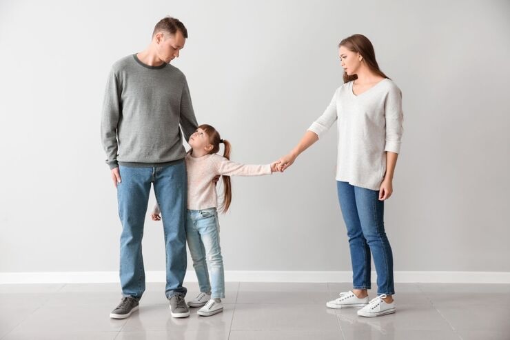 Mamma tiene per mano figlia che abbraccia gamba del papà