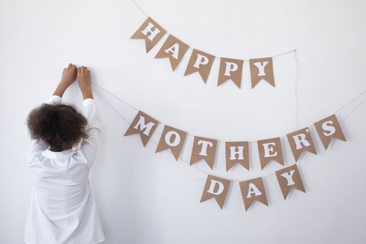 Bambina di spalle appende striscione con scritto "Happy Mother's day"