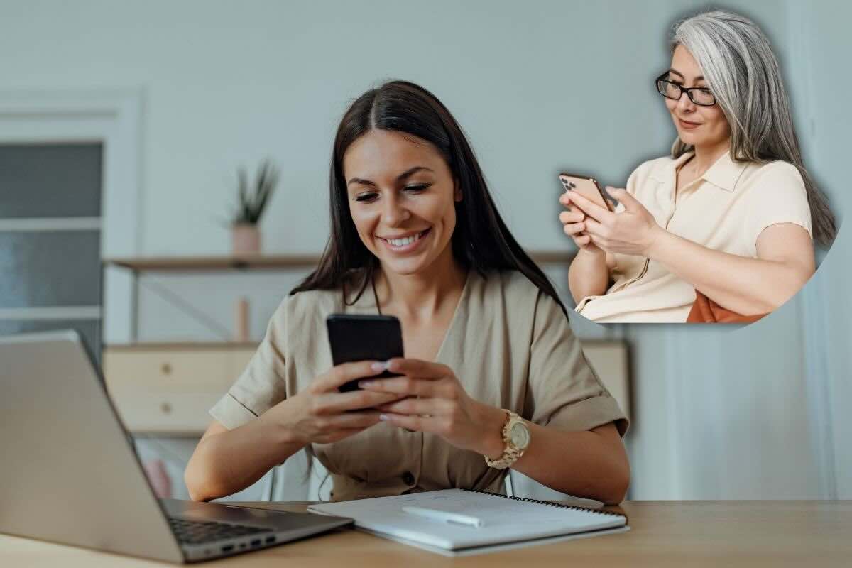Ragazza alla scrivania sorridente con smartphone e in alto donna matura che legge messaggio sullo smartphone, felice