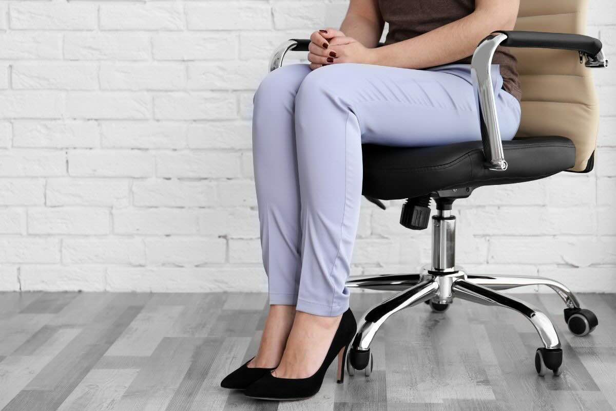 Donna seduta su sedia di ufficio si tiene le mani sulle gambe