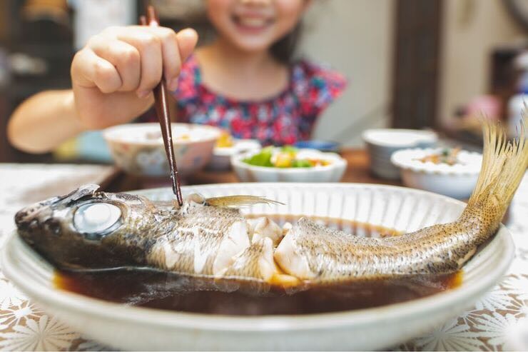 Mani di bambina sorridente che con una forchetta infilza pesce