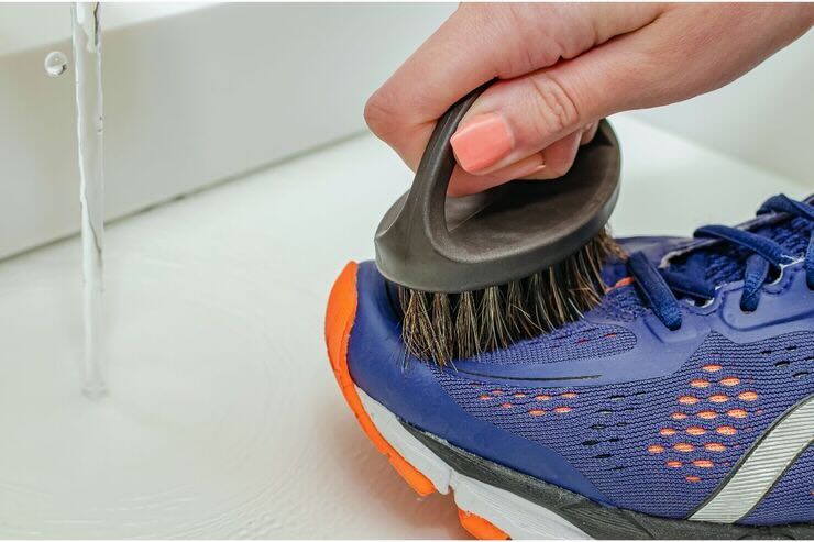 Mano con smalto arancione spazzola scarpe da ginnastica blu-viola con suola bianca e arancione