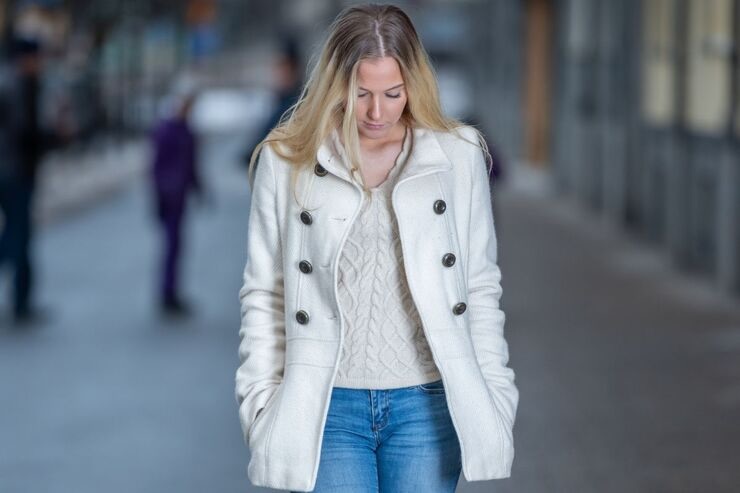 Ragazza con cappotto e maglione bianchi, cammina guardando a terra
