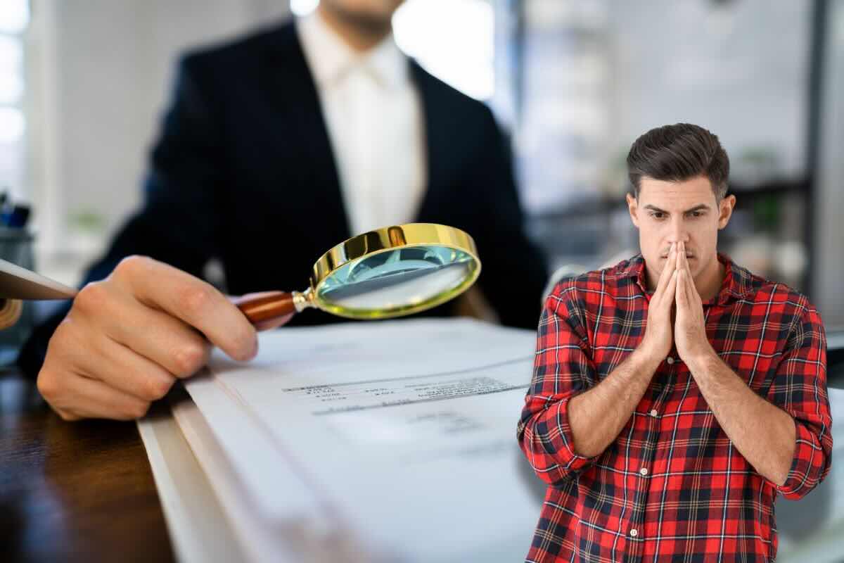 Persona con lente di ingrandimento su documento, uomo in primo piano con mani sul viso, preoccupato