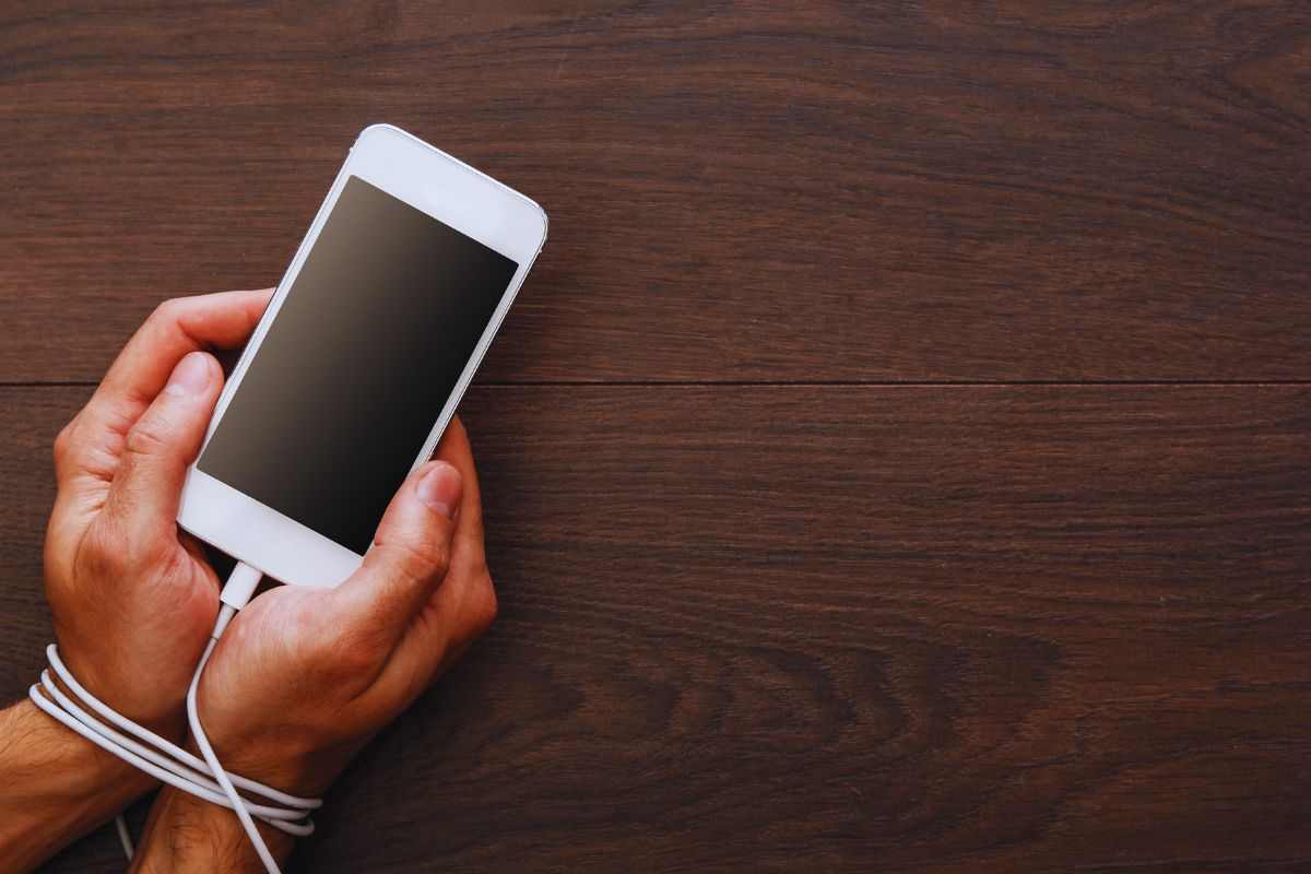 Persona con le mani legate allo smartphone dal cavo di ricarica