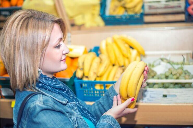 Donna guarda casco di banane al reparto frutta del supermercato