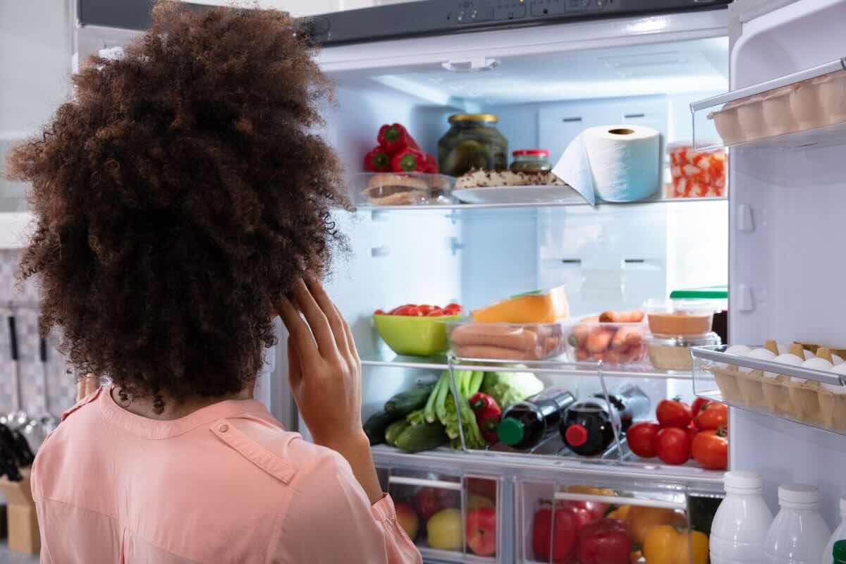 Ragazza guarda nel frigorifero pieni di alimenti e rotolo carta igienica