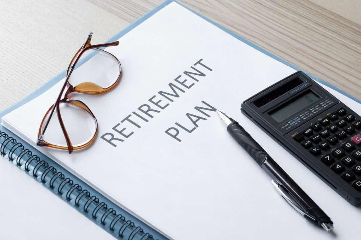 Quaderno con scritto "Retirement plan", occhiali da vista, penna, calcolatrice
