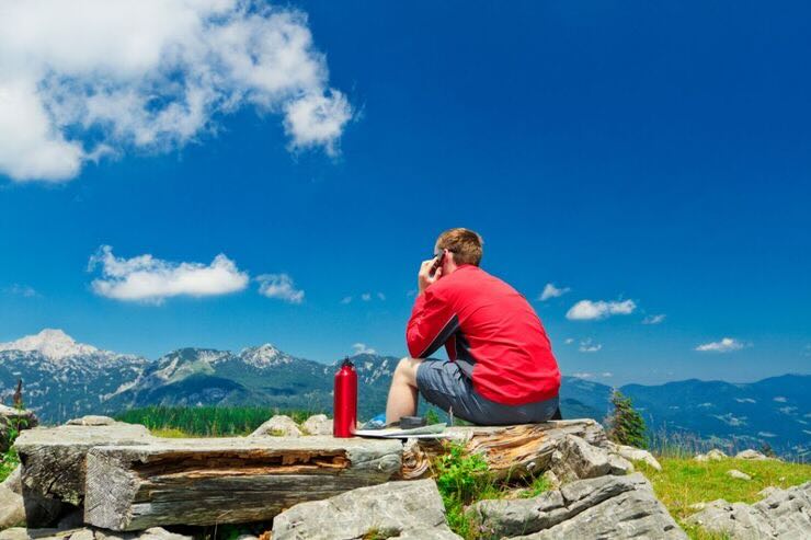 Ragazzo seduto di spalle con telefono all'orecchio immerso nella natura