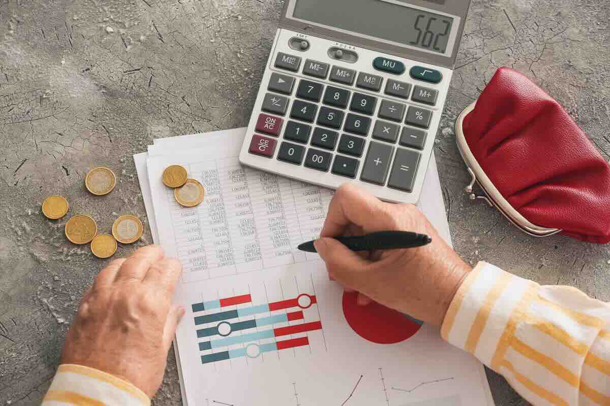 Calcolatrice, documento, grafici, monete, mano scrive con la penna
