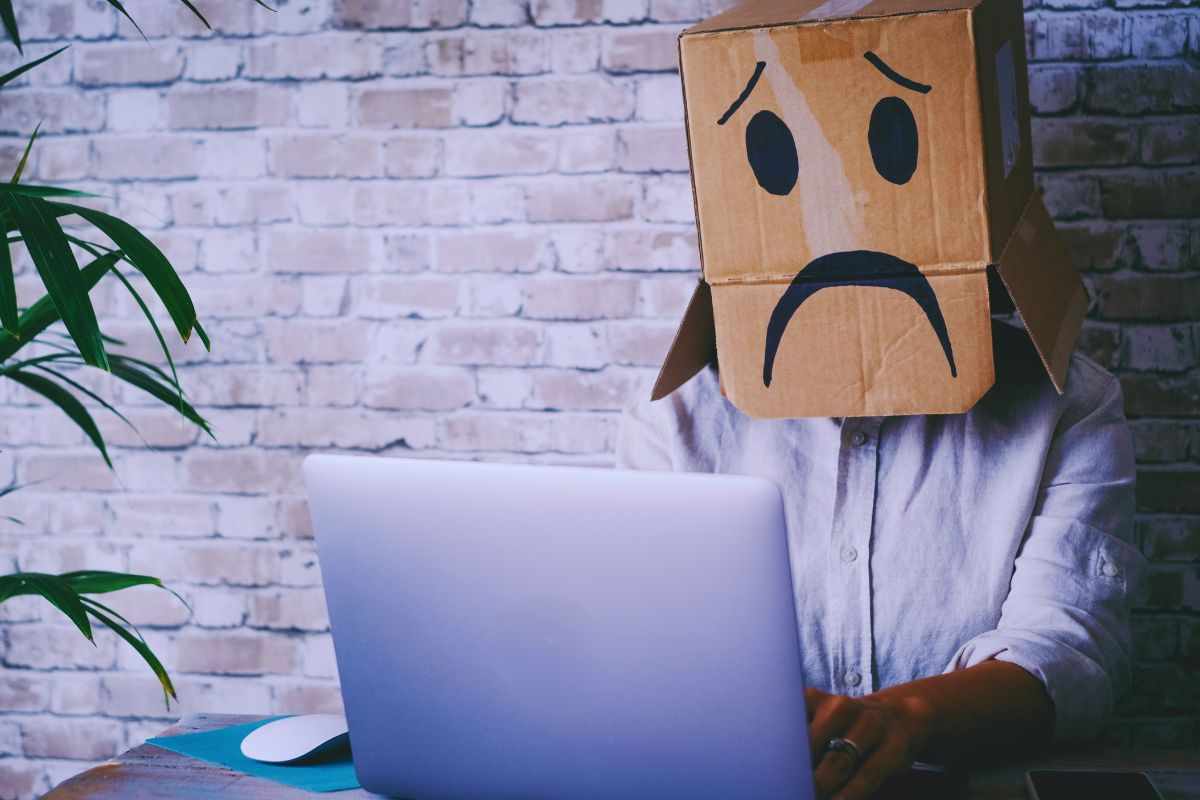 Uomo al PC con in testa un cartone raffigurante uno emoticon triste