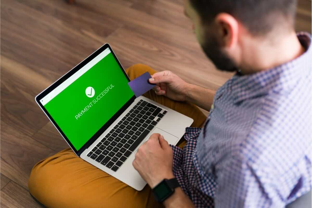 Uomo guarda schermata verde su PC cn carta in mano, c'è scritto "pagamento riuscito" in inglese