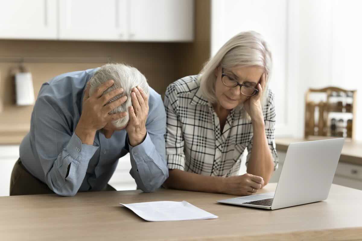 Due pensionati leggono un foglio, lui con mani sulla testa