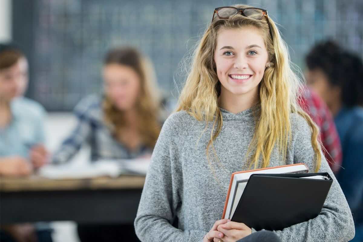 Ragazza sorridente in aula con libri, sul fondo un'altra persona