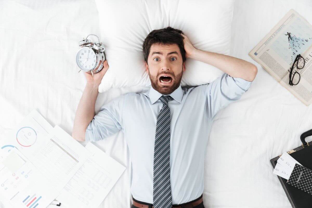 Uomo nel letto grida, sveglia in mano, fogli sparsi sulle lenzuola