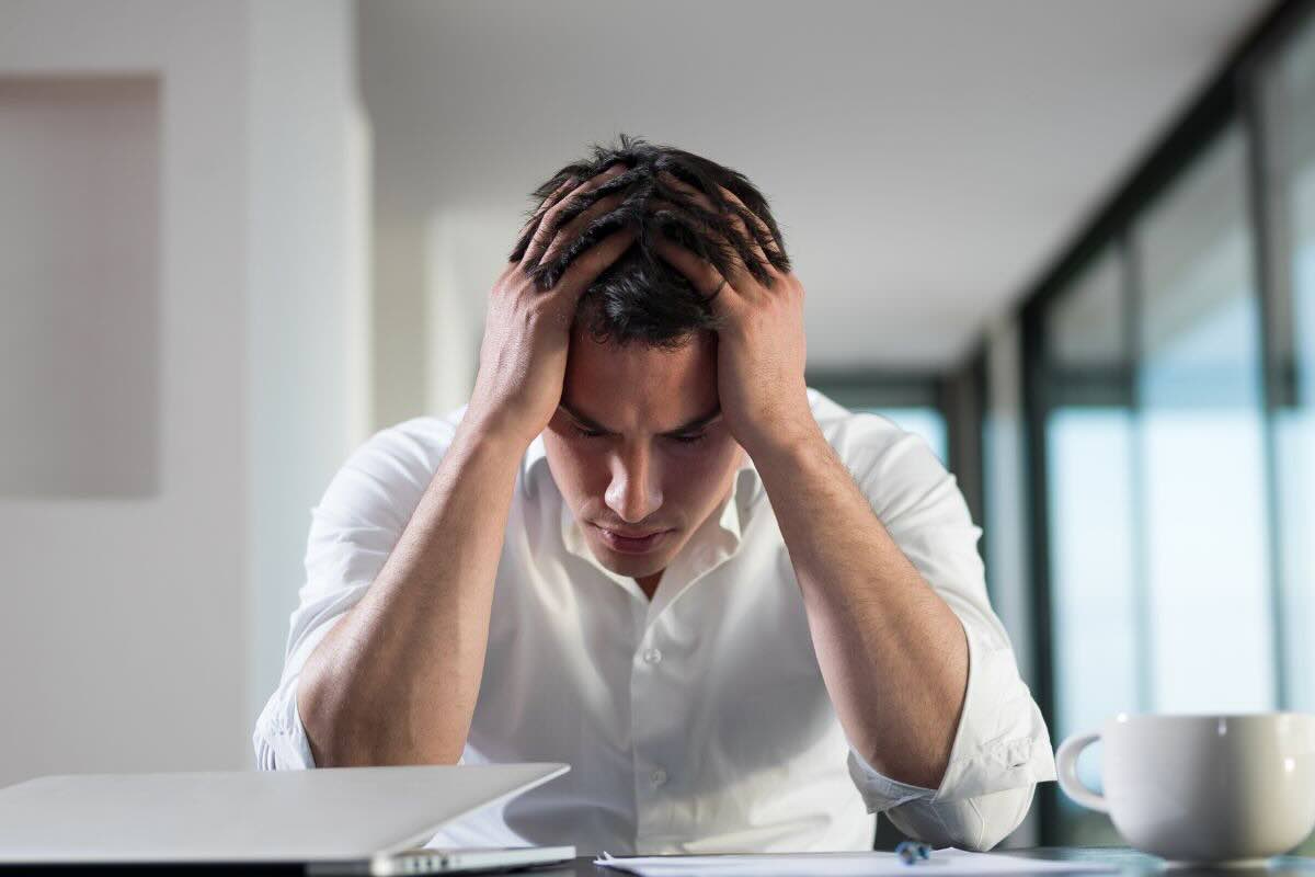 Uomo con mani nei capelli seduto alla scrivania