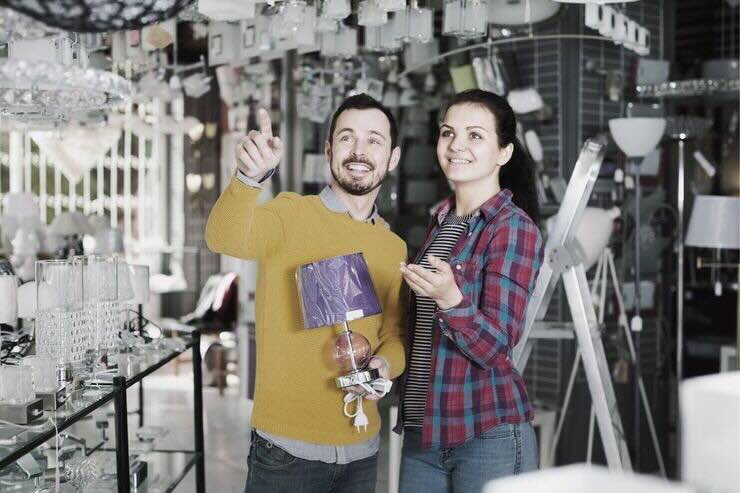 Coppia nel reparto illuminazioni di un negozio, lui ha in mano una lampada da comodino