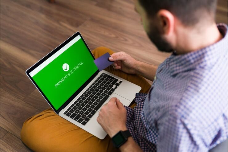 Uomo al PC fa bonifico, carta in mano