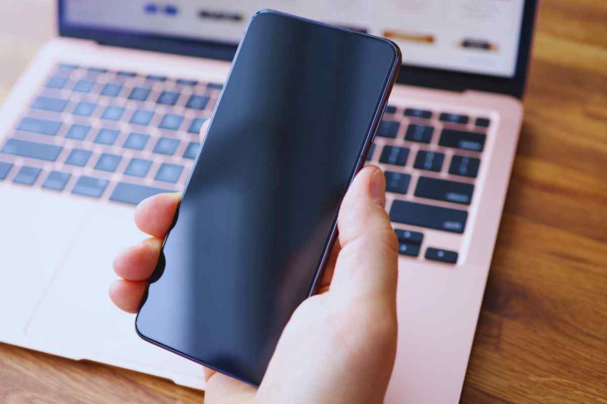 Persona che tiene in mano uno smartphone e laptop sullo sfondo