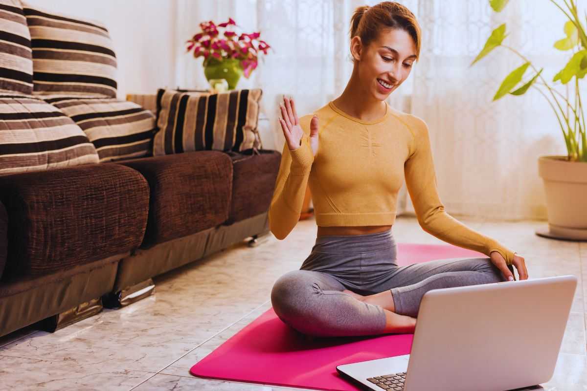 Donna che si allena a casa facendo una lezione di yoga online