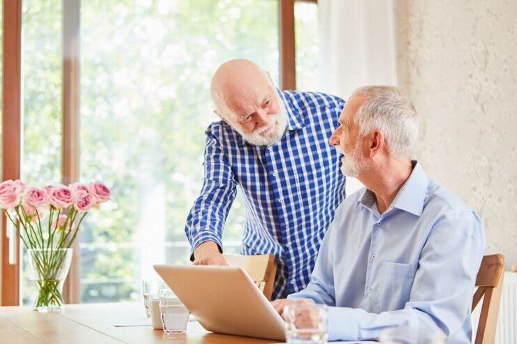 Due anziani chiacchierano, uno seduto al PC